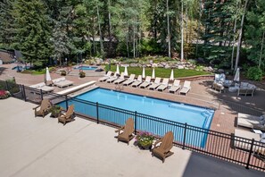 Une piscine entourée d’une clôture et de verdure, avec des chaises longues et des parasols.