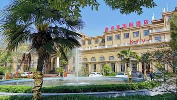 A hotel with a fountain, palm trees, and a clear blue sky.