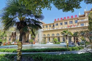 A hotel with a fountain, palm trees, and a clear blue sky.