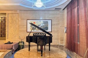 Un piano de cola en una habitación con piso de mármol, una araña y una obra de arte enmarcada en la pared, junto con una cortina roja.