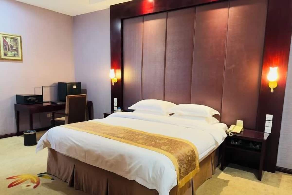 Une chambre d’hôtel avec un grand lit, un bureau, une chaise, un téléphone et un luminaire fixé au mur.