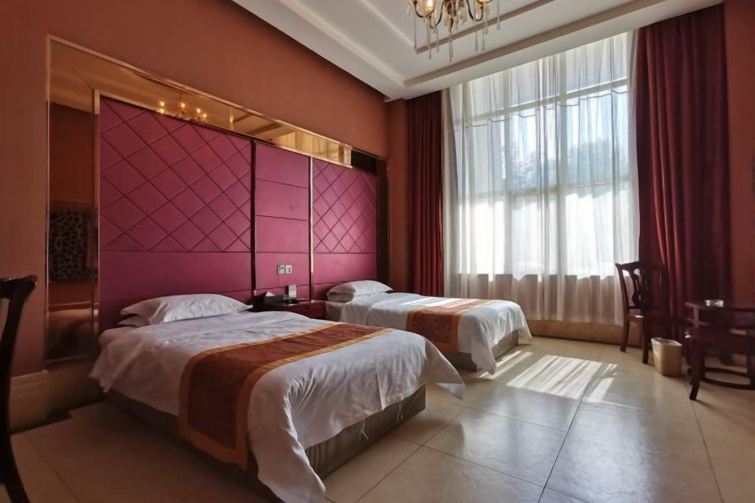 Habitación de hotel con dos camas, un ventanal con cortinas, un candelabro y una silla de madera.