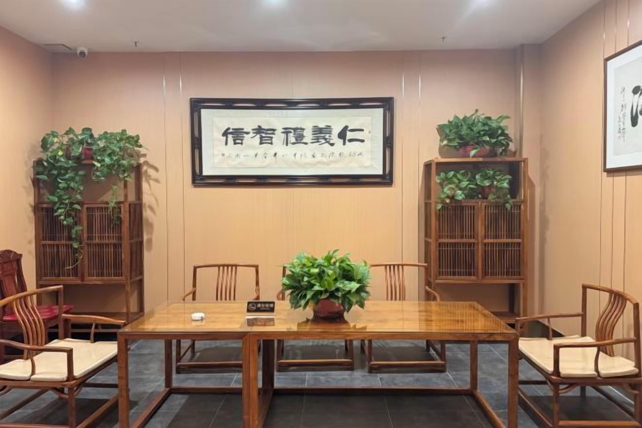 A conference room with a long table, chairs, potted plants, and framed text on the wall.
