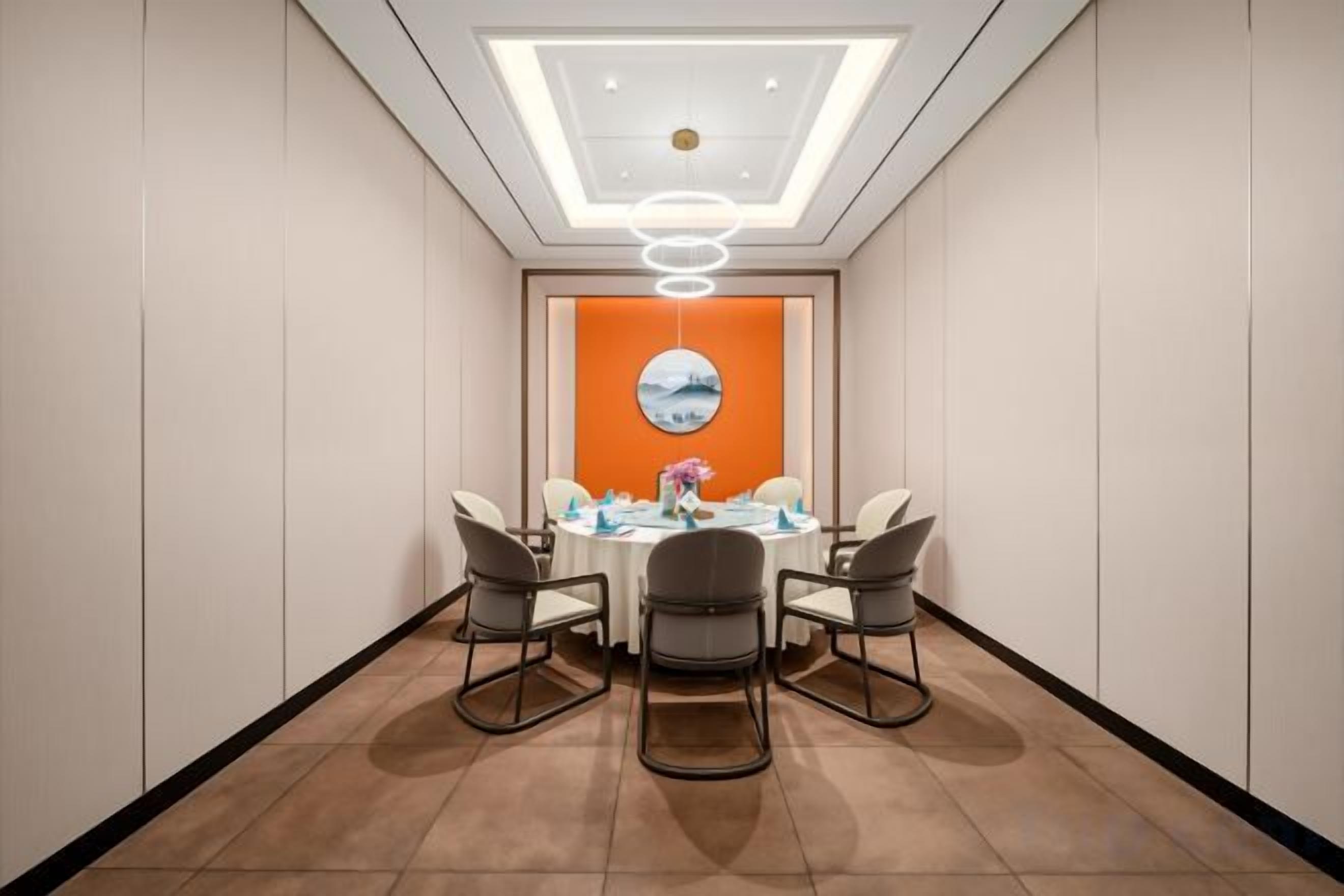 A conference room with a round table, four chairs, a modern ceiling light, and a wall-mounted clock.
