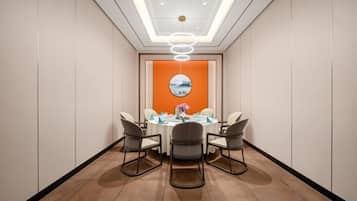 A conference room with a round table, four chairs, a modern ceiling light, and a wall-mounted clock.