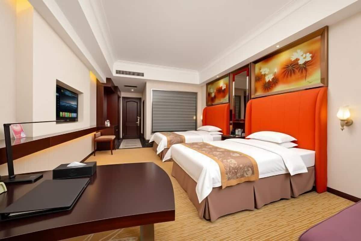 Une chambre d’hôtel avec deux lits, un bureau, une chaise, une télévision et des œuvres d’art accrochées aux murs.