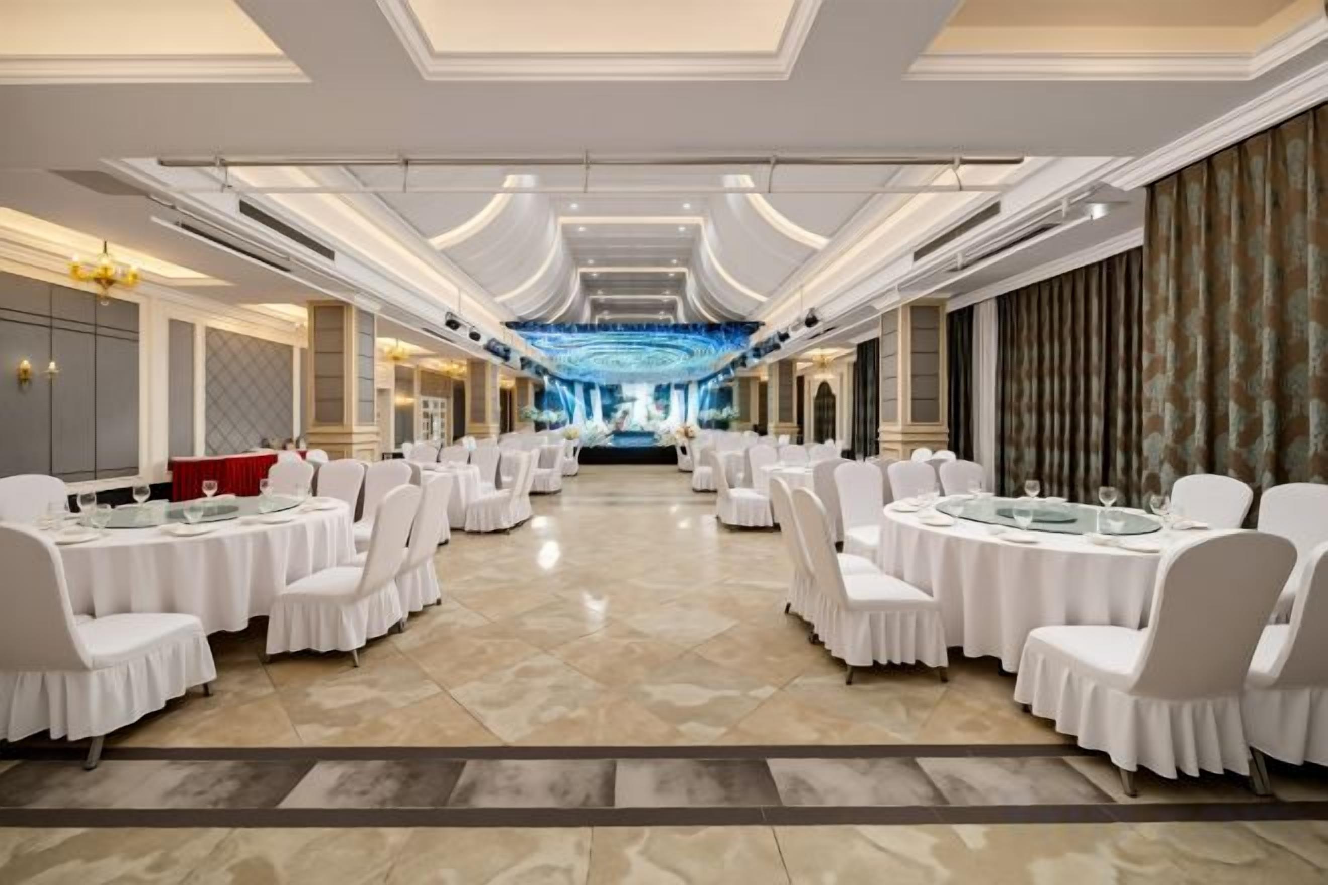 A banquet hall with round tables and chairs, a chandelier, and a large screen at the front.