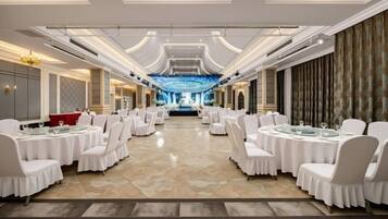 A banquet hall with round tables and chairs, a chandelier, and a large screen at the front.