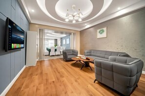 A modern living room with a sectional sofa, a flat-screen TV mounted on the wall, and a wooden floor. - Jinshawan International Hotel (Weishi)