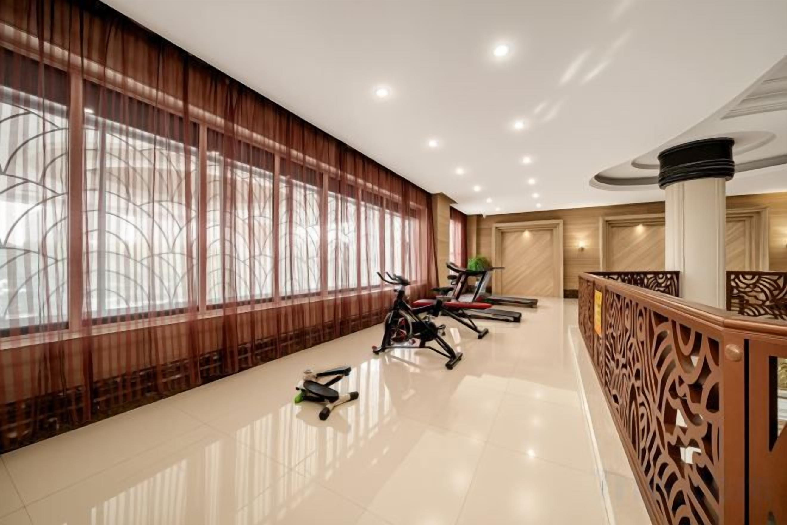 A spacious hotel lobby with exercise equipment, large windows, and a decorative railing.