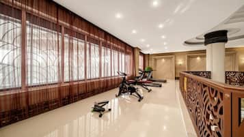 A spacious hotel lobby with exercise equipment, large windows, and a decorative railing.