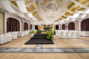 A banquet hall with a central stage, white round tables, and a chandelier.