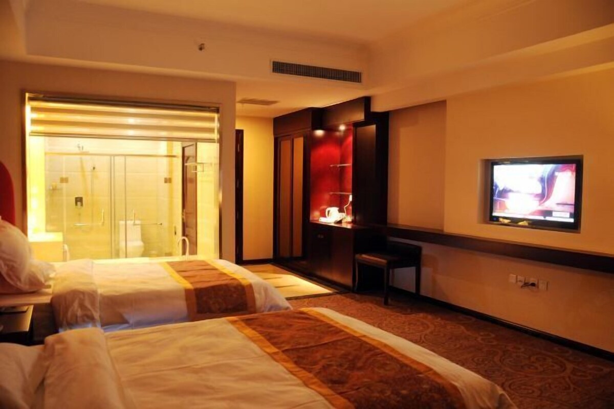 A hotel room with two beds, a television, a desk, and a bathroom visible through an open door.