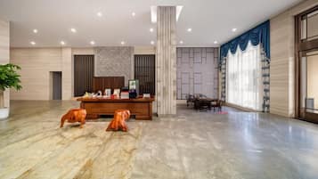 A spacious lobby with a reception desk, seating area, and a large window with curtains.