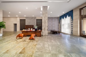 Un vestíbulo amplio con una recepción, zona de estar y un gran ventanal con cortinas.