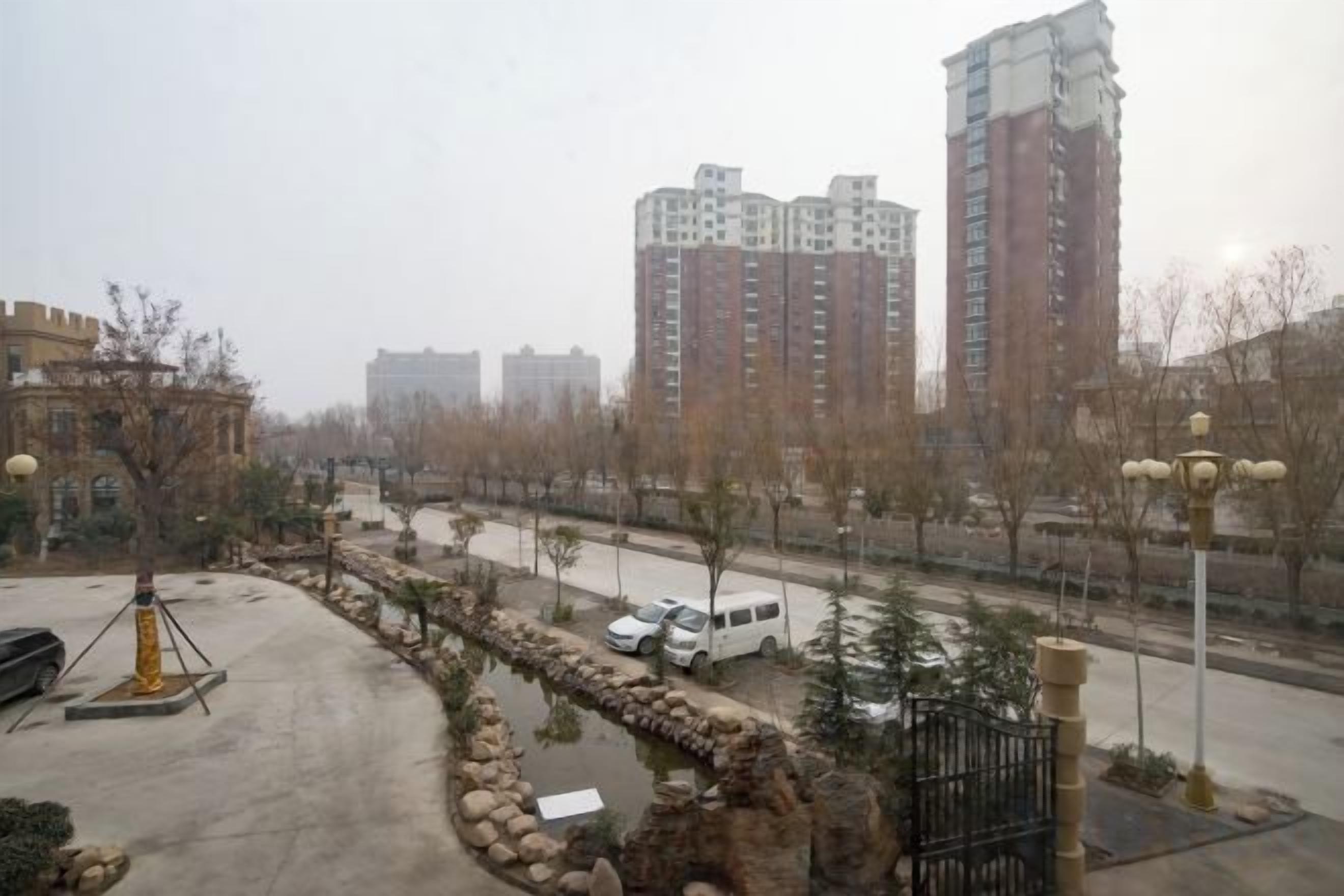 A residential area with high-rise buildings, a paved road, and a small water feature.