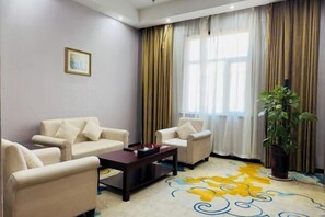 A living room with beige sofas, a dark coffee table, and a colorful carpet. - Jinshawan International Hotel (Weishi)