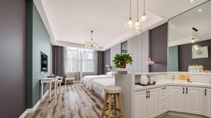 Een moderne hotelkamer met een houten vloer, een bed, een bureau, een stoel, een grote spiegel en een kitchenette.
