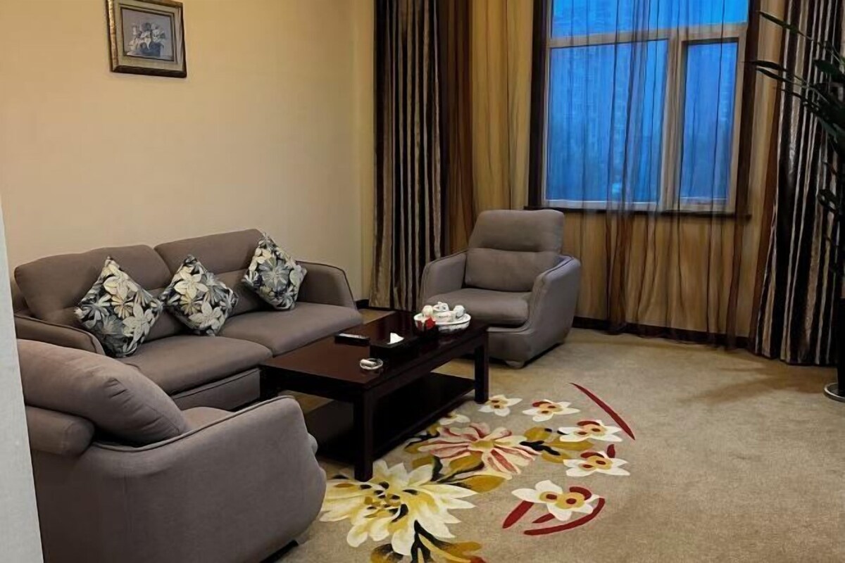 A living room with a sofa, armchair, coffee table, and a floral rug.