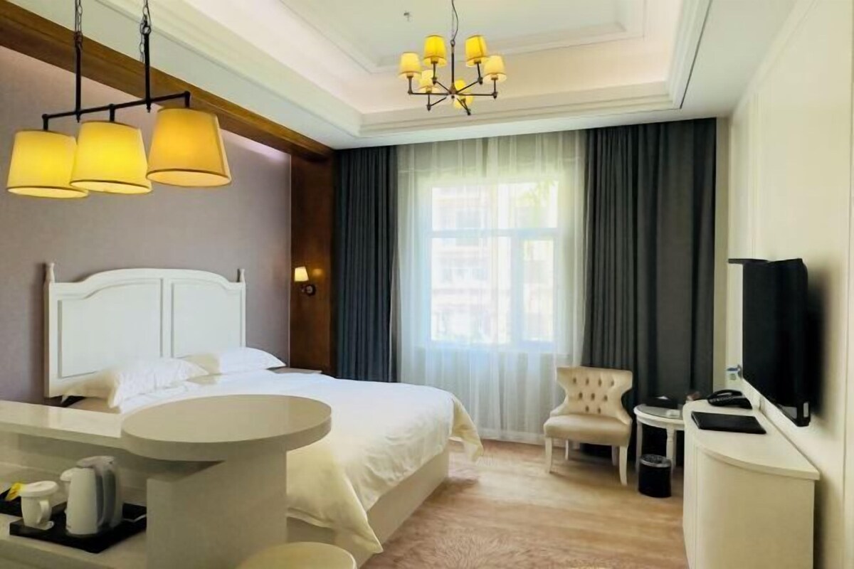 A hotel room with a bed, a round table with a coffee maker, a TV, and a chair.
