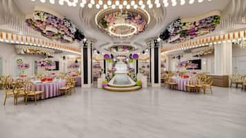 A spacious banquet hall with multiple round tables, elegant chandeliers, and floral decorations.