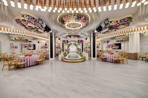 Une salle de banquet spacieuse, dotée de nombreuses tables rondes, de lustres élégants et de décorations florales.