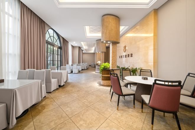 A hotel dining area with multiple tables and chairs, a large pillar, and a wall with a logo.