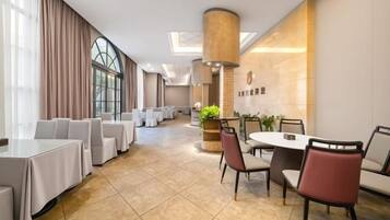 A hotel dining area with multiple tables and chairs, a large pillar, and a wall with a logo.