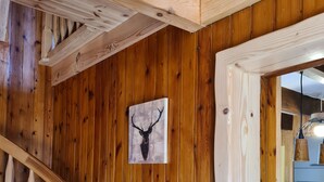 A wooden interior with a spiral staircase, a mounted deer head artwork, and a kitchen area visible through an open doorway. - Lake view chalet (Matemale)