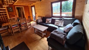 A wooden cabin interior with a sofa, chairs, a table, and a staircase. - Lake view chalet (Matemale)