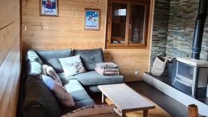 A cozy cabin interior with a wooden ceiling, a stone wall, a sofa, a table, and a fireplace. - Lake view chalet (Matemale)