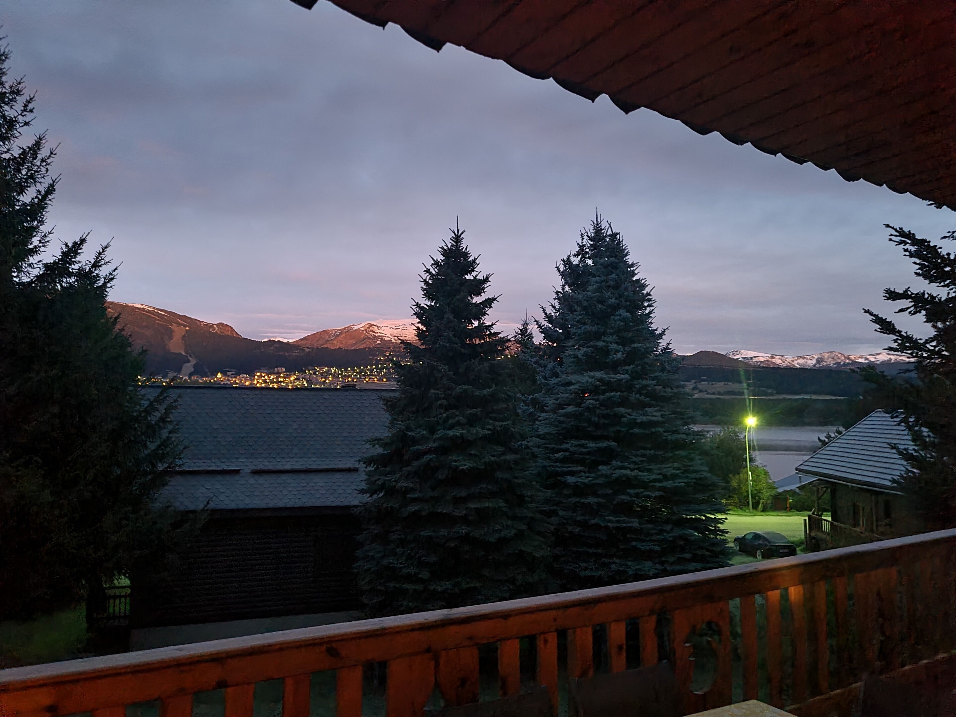 A view from a balcony overlooking a lake with snow-capped mountains in the background and a town with lights.