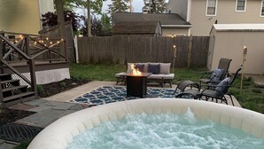 Ein aufblasbarer Whirlpool in einem Garten mit Feuerstelle, einer Terrasse mit Gartenmöbeln und einem Holzboden.