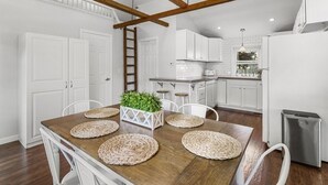 Eine moderne Küche mit weißen Schränken, einem Holztisch mit gewebten Tischsets und einem Kühlschrank aus Edelstahl.