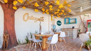 Un restaurante con una mesa de madera y sillas blancas, una gran escultura de árbol, y una pared con la palabra 'Café'.