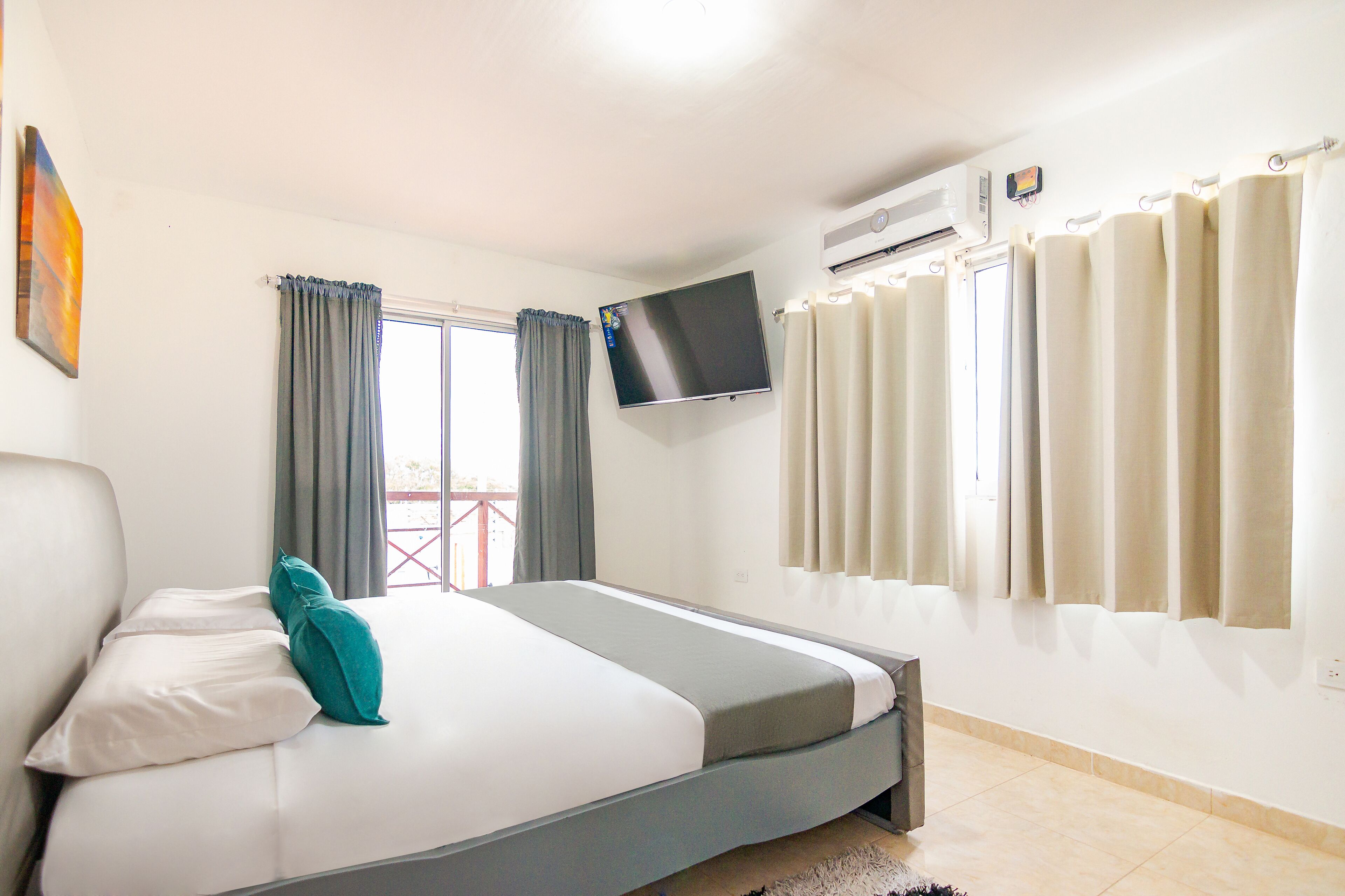 A bedroom with a bed, a TV mounted on the wall, and an air conditioning unit.
