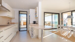 Una cocina moderna con armarios blancos, una zona de comedor con una mesa redonda y sillas, y vistas al balcón a través de puertas correderas amplias.