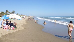 Una playa con gente, sombrillas y cielo despejado.