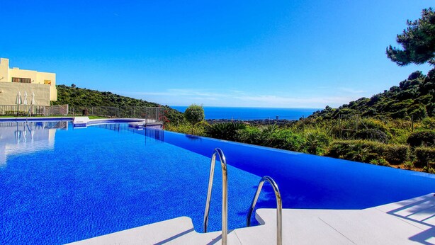 Una piscina infinita de color azul intenso con escaleras de metal, rodeada de exuberante vegetación y vistas al mar.