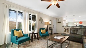 Een woonkamer met een plafondventilator, twee turquoise fauteuils, een salontafel, een bank en een vloerkleed.