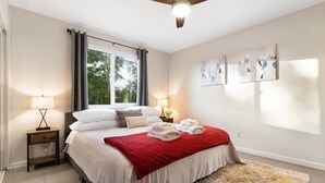 Een slaapkamer met een bed, twee nachtkastjes, een plafondventilator en kunst aan de muur.