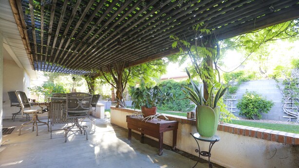 En udendørs patio med pergola, siddepladser og krukkeplanter.