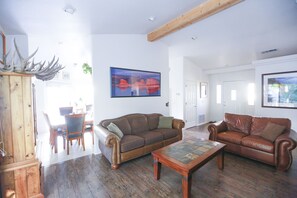 A spacious living room with two leather sofas, a wooden coffee table, and a dining area with a wooden cabinet and chairs.