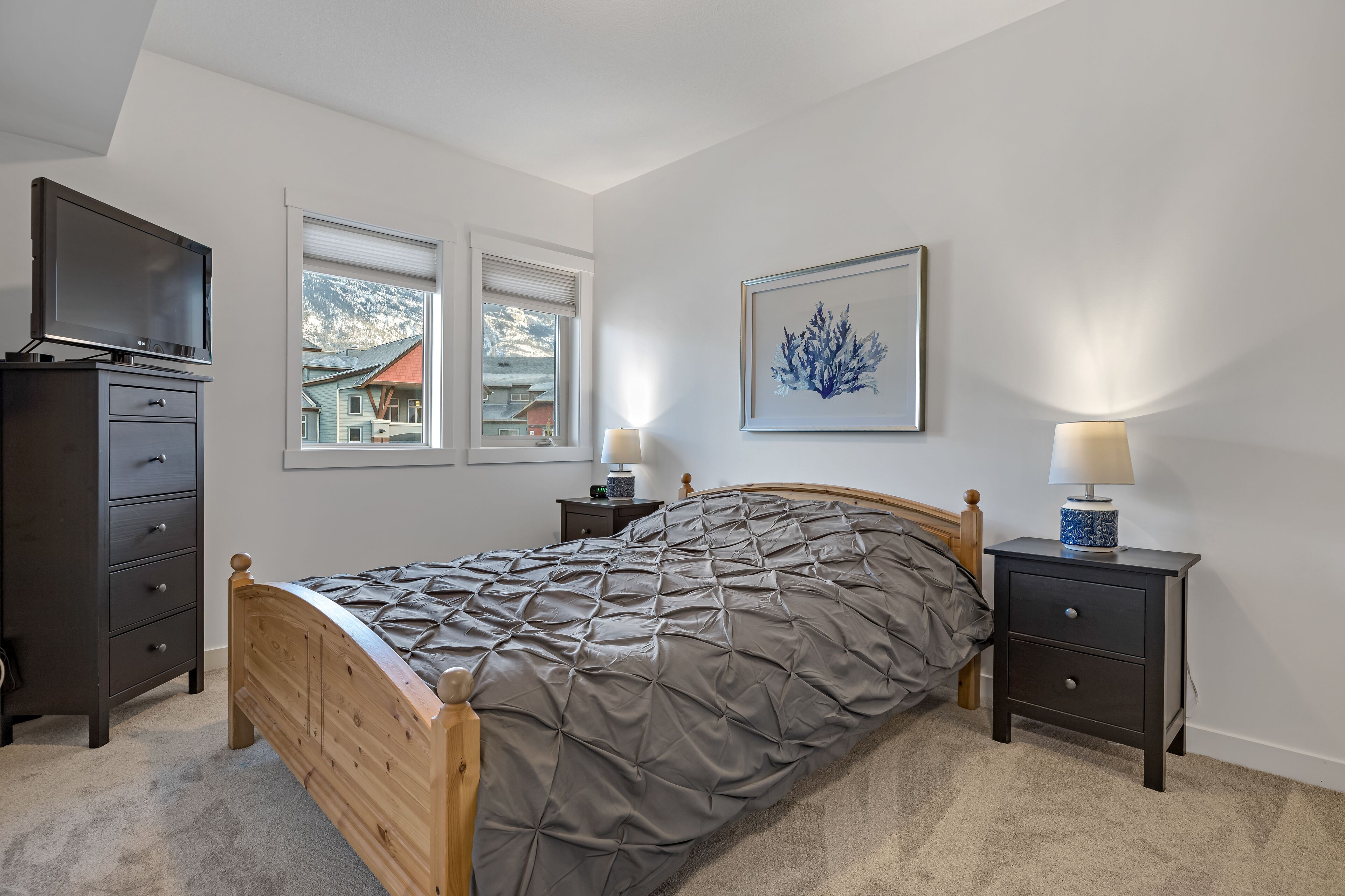 A bedroom with a bed, a TV, a dresser, a nightstand with a lamp, and a framed picture on the wall.