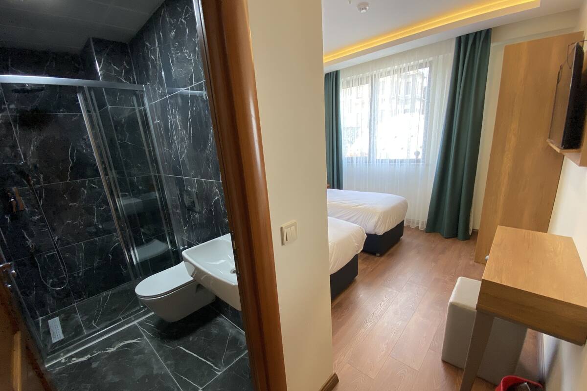 A hotel room with a shower, toilet, bed, and a small table.