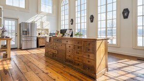 Eine geräumige Küche mit Holzboden, einer großen Insel mit Schubladen, einem Kühlschrank und einem Fenster mit Blick ins Freie.