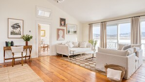 Ein geräumiges Wohnzimmer mit Holzboden, einem weißen Sofa, einem Couchtisch und Blick auf eine verschneite Landschaft durch große Fenster.