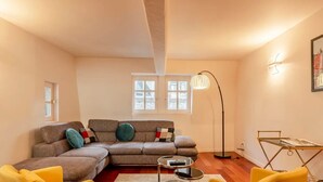 A living room with a sectional sofa, a floor lamp, a small table, and a magazine rack.