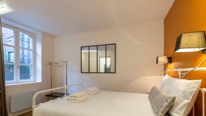 A hotel room with a bed, bedside table, lamp, window, and a mirror on the wall.