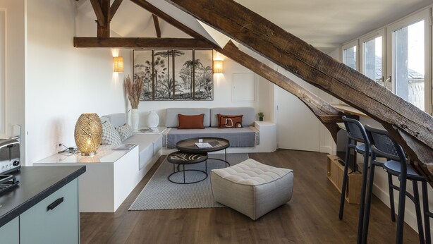 Ein modernes Wohnzimmer mit einer Holztreppe, einer Sofagarnitur, einem Couchtisch und einem Essbereich mit Stühlen.